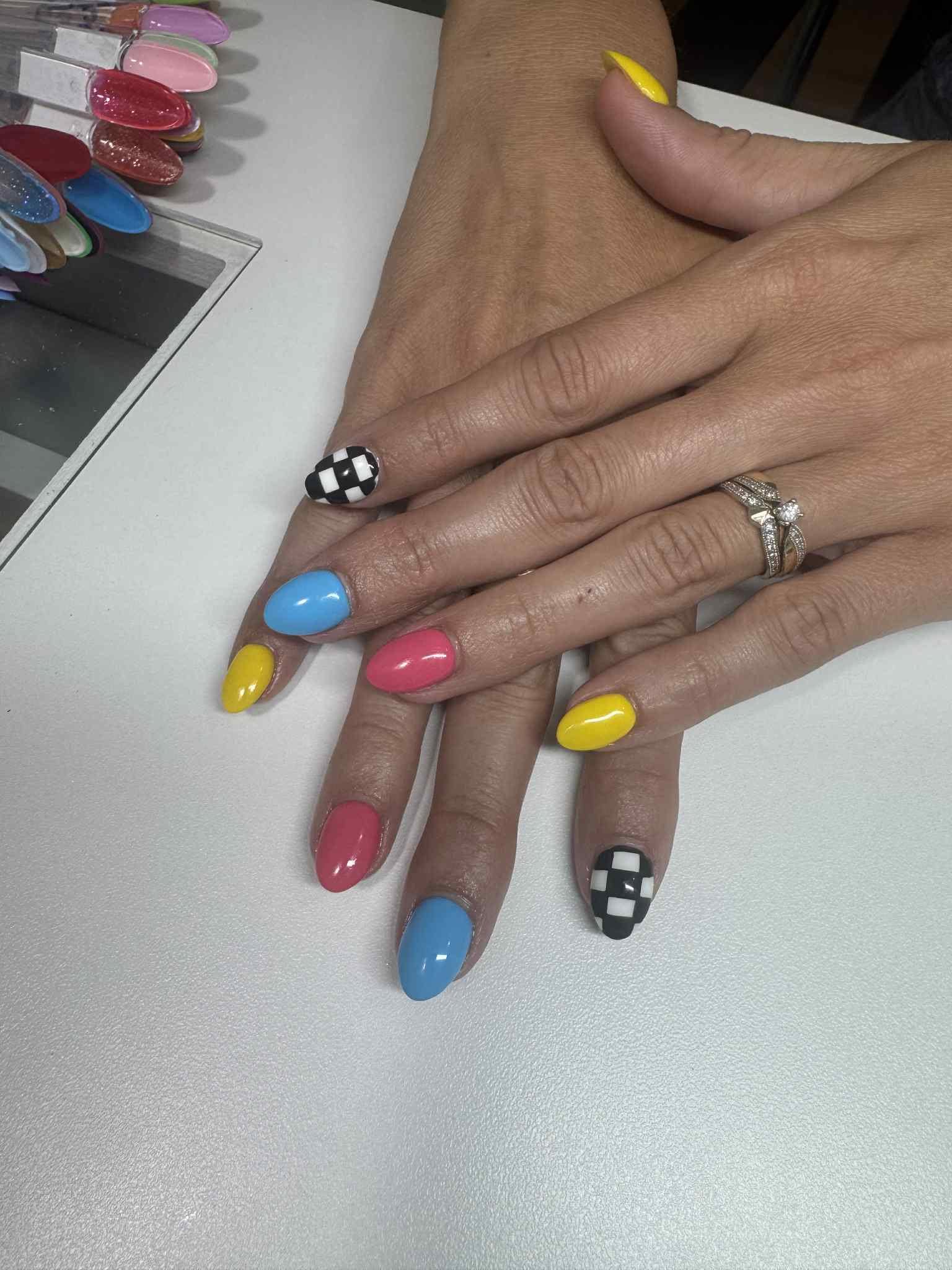 Pose d'ongles colorée, vernis bleu, jaune et corail avec ongle damier noir et blanc